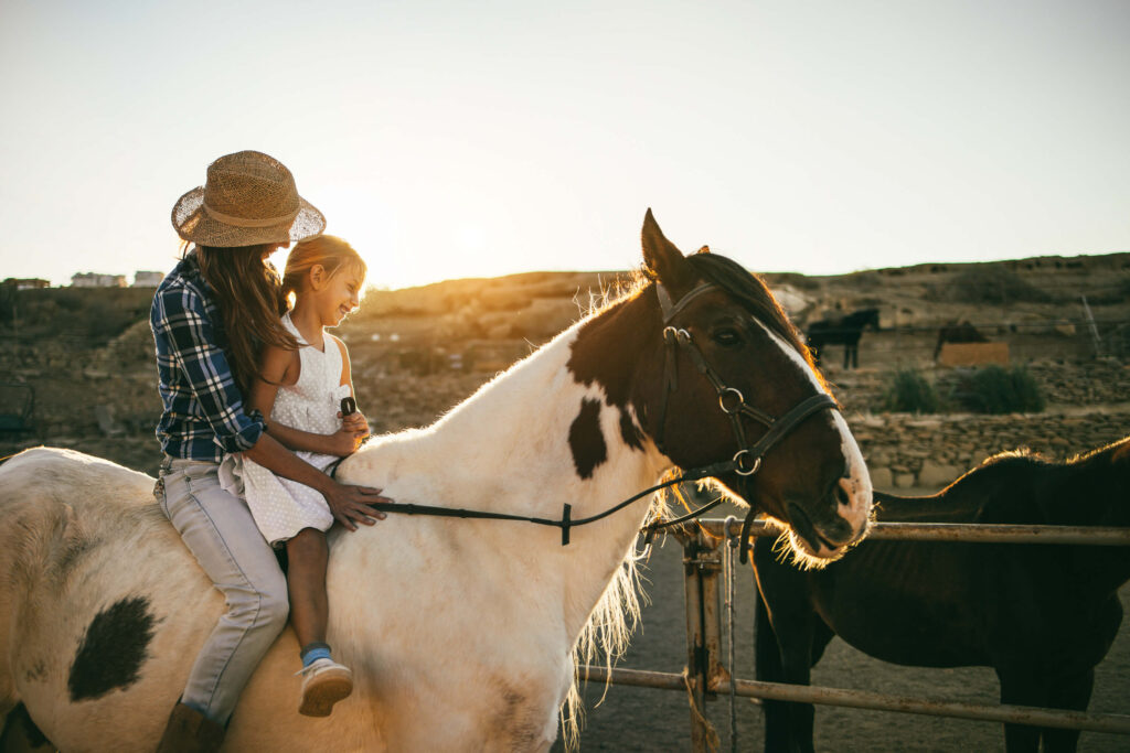 Happy mother and daughter riding a horse at sunset